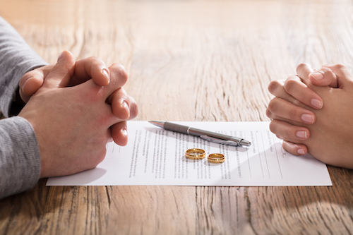 Hands Of Wife And Husband On Divorce Document With Wedding Ring In The Center