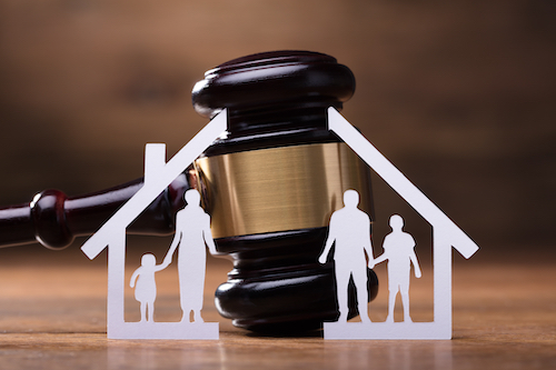 White Family Paper Cut Out In Front Of Judge Gavel On The Wooden Desk