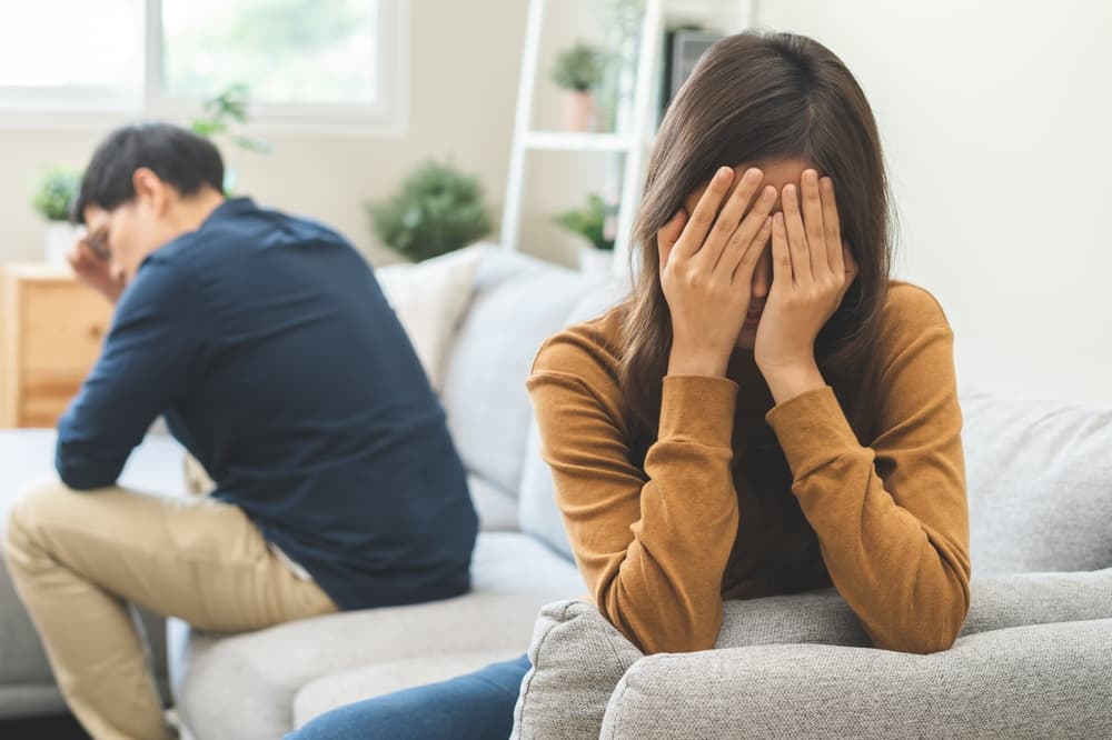 A young couple argues, with the wife looking upset and the husband appearing frustrated, reflecting tension and emotional distress in their troubled relationship.