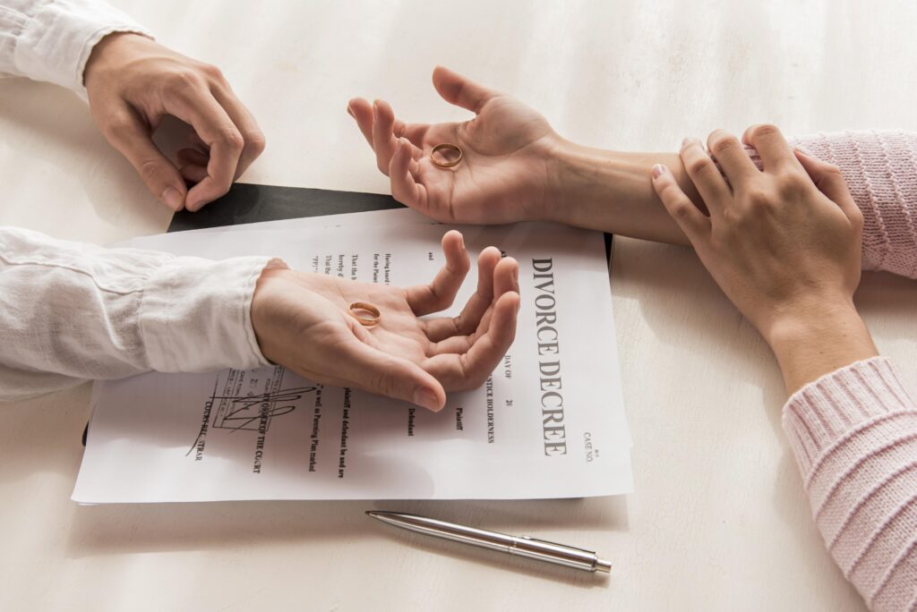 High-angle photo of hands holing rings with divorce paperwork under them