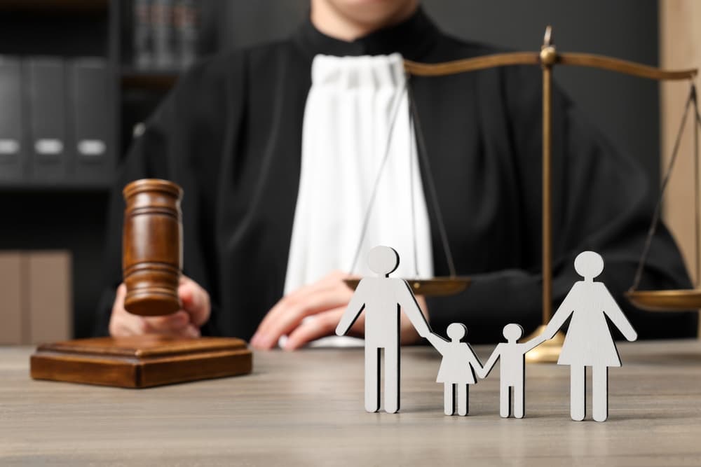 Family law. Judge with gavel and scales of justice sitting at wooden table, focus on figure of parents and children