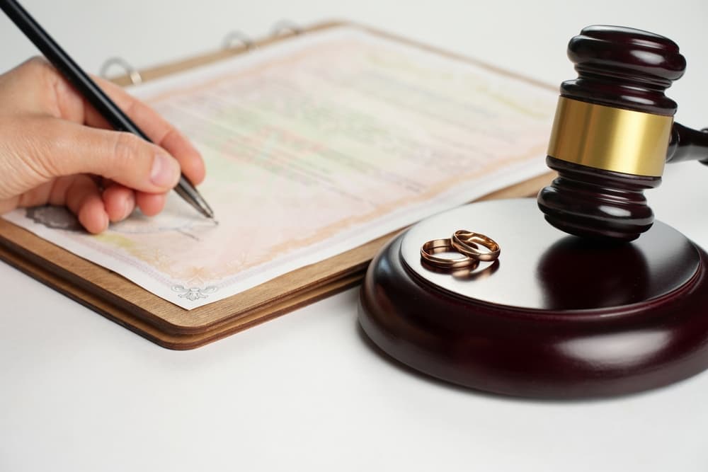 Woman hand signing divorce contract. Wedding rings with marriage contract and judge gavel