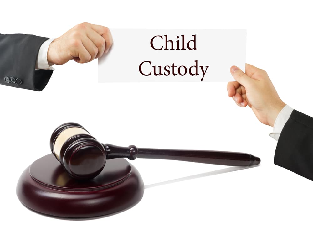 Wooden judges gavel on table in a courtroom. Lawyer Hands holding card with text Child Custody.