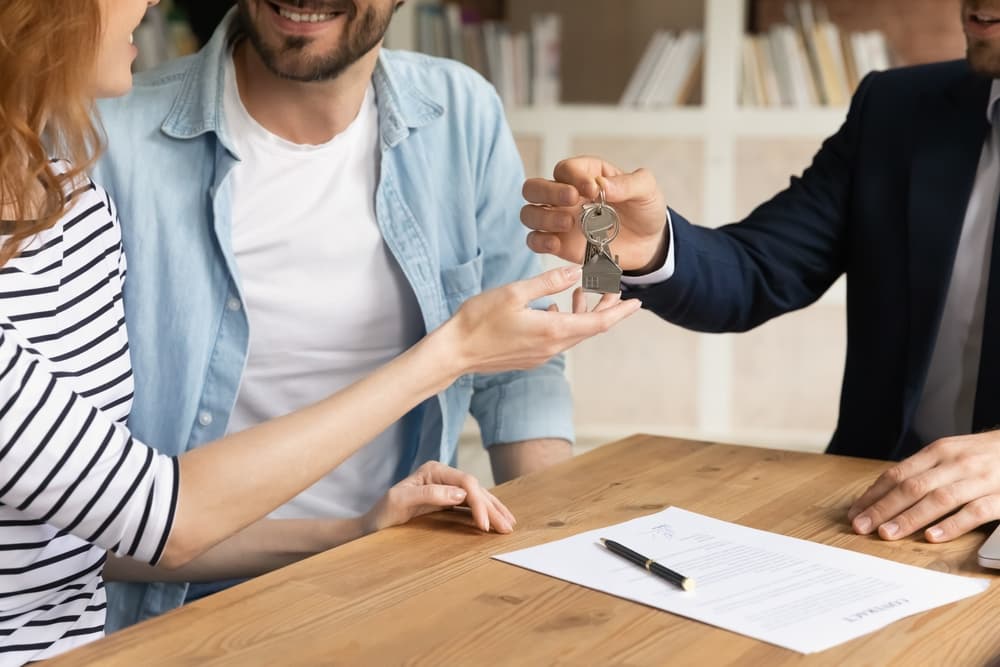 An unmarried couple receiving keys from new own property, finish meeting in real estate agency lead by realtor in formal suit.