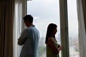 Silhouette of an Asian couple having a serious argument, turning away from each other by the window at home.