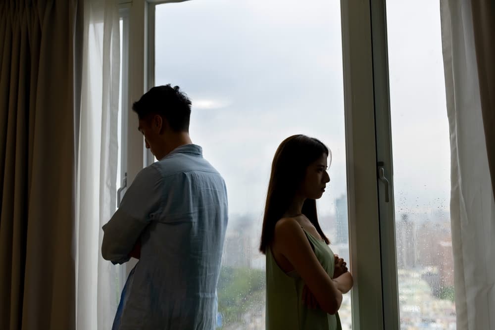 Silhouette of an Asian couple having a serious argument, turning away from each other by the window at home.