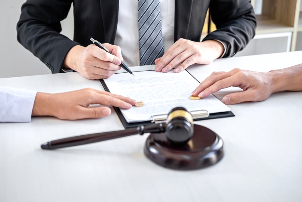 A lawyer prepares the divorce agreement as a husband and wife sign the decree of dissolution, symbolizing the legal conclusion of their marriage with the guidance of a legal professional or counselor.