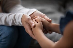 Close-up of an adult gently holding a child's hands, representing care, support, and family connection in a legal or emotional context.